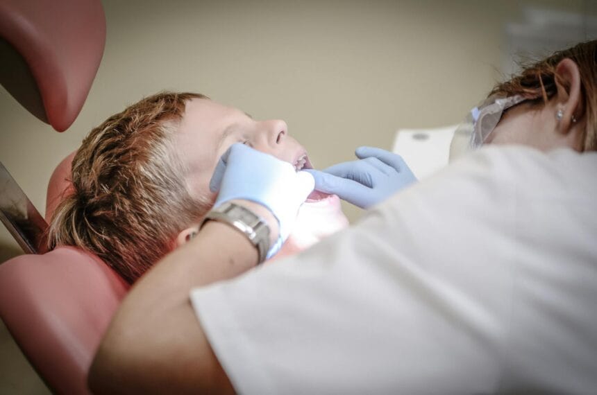 dentist woman wearing white gloves and white scrubsuit checking boy s teeth