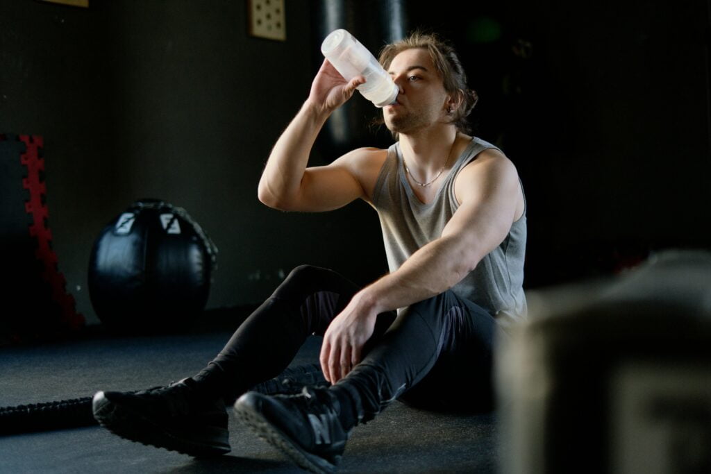 A man sitting on the floor, drinking water out of a bottle